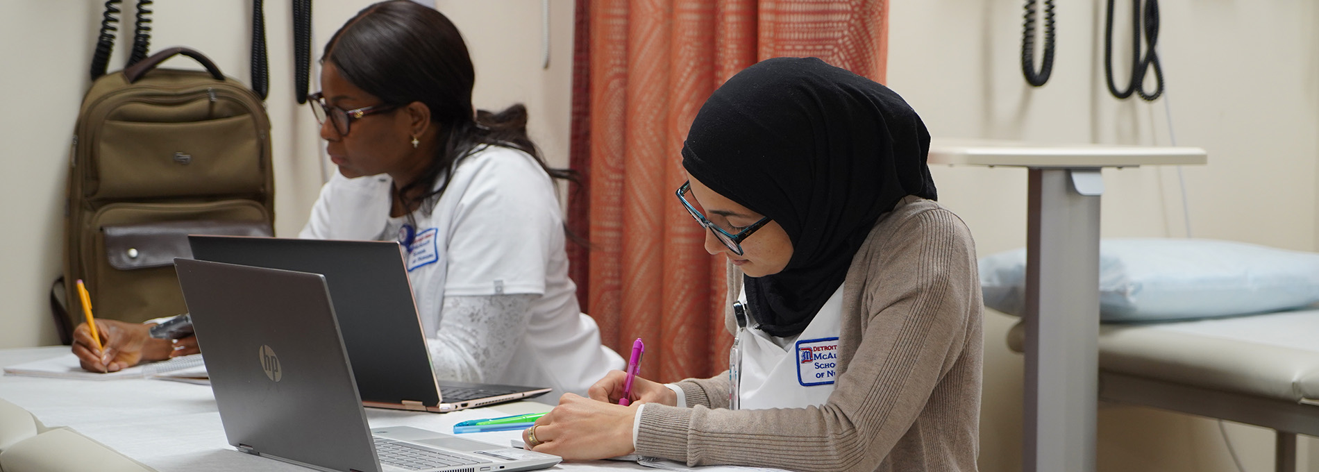 Detroit Mercy healthcare students write and work on their laptops at a table.