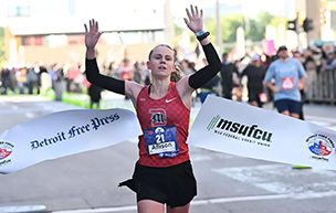 Allison Sherman '24 raises her arms in celebration as she crosses the finish line to win the Detroit Free Press Marathon.